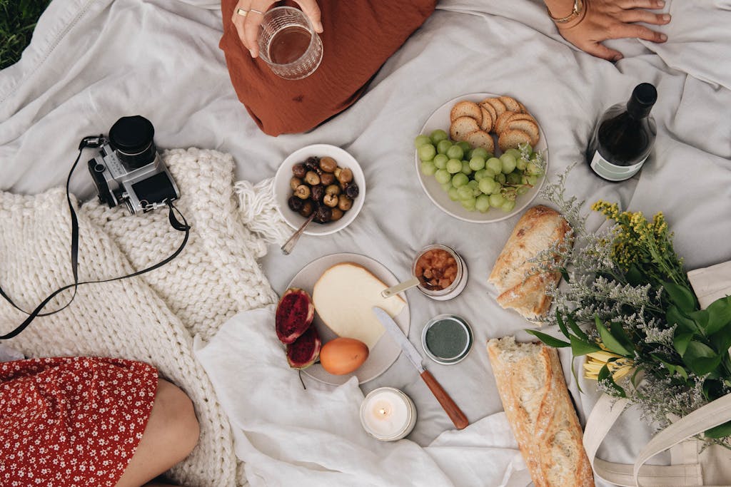 Top view of a cozy picnic with snacks, wine, cheese, bread, grapes, and a retro camera.